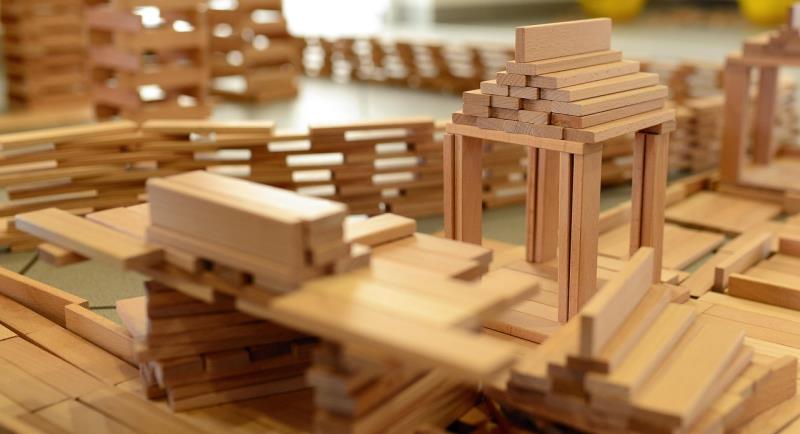 Piles of play-sized short wooden building planks, some built into walls and some in a tower. 