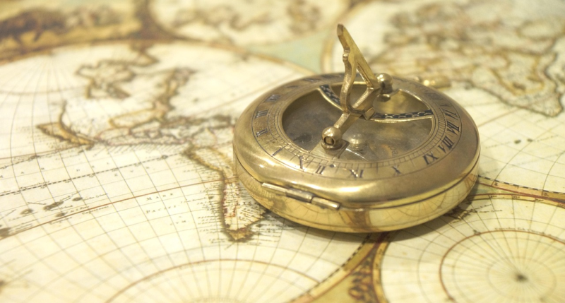 A vintage brass sundial compass rests on an antique world map, evoking a sense of exploration and adventure. The map's sepia tones enhance the nostalgic mood.